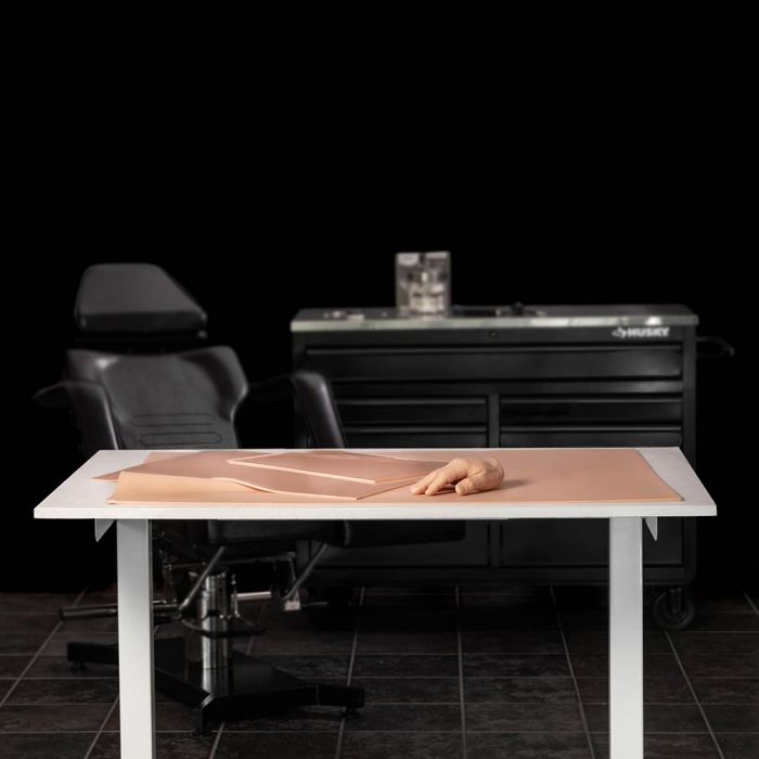 Black-themed tattoo studio with a white table. A variety of tattooable flesh products are spread out on the table.