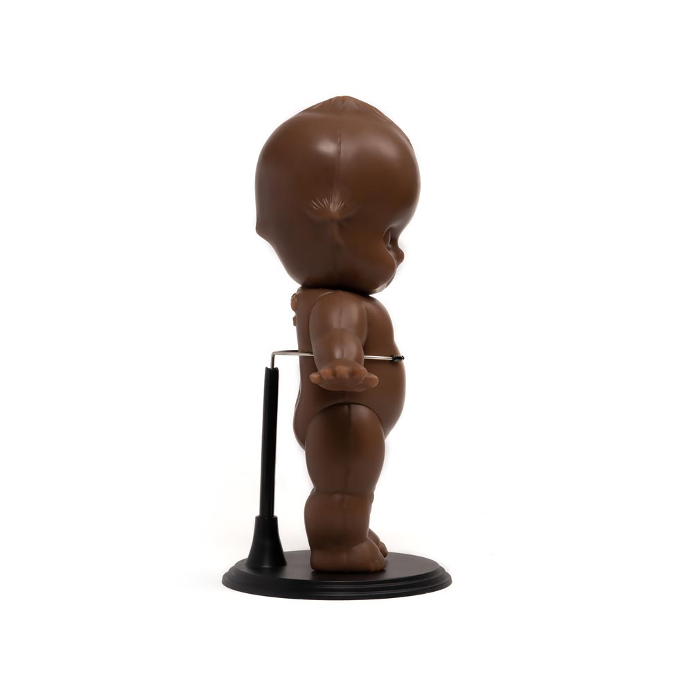 Dark-toned tattooable cutie doll on a black stand side-facing with a white background.