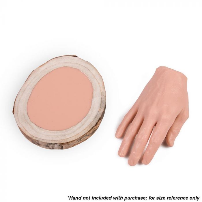 Tattooable flesh imbedded in a frame that looks like a wooden slab from the branch of a tree. This product is posed in front of a white background next to a tattooable hand.